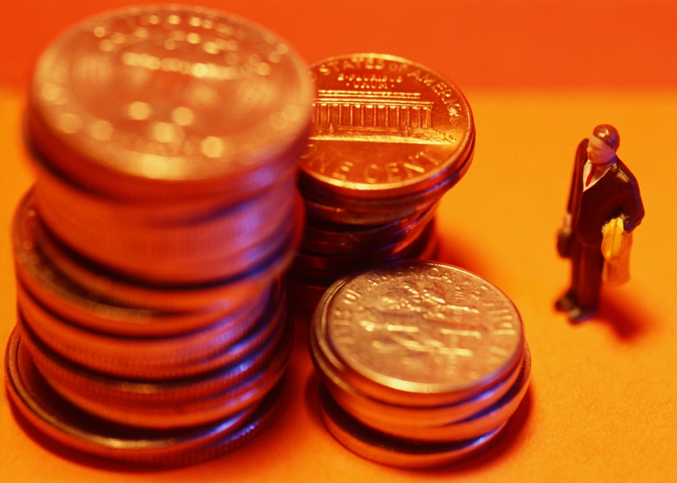 Toy Person Looking At Stacks of Coins