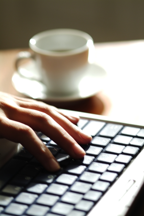 Hands Working on a Laptop Computer with Coffee Cup