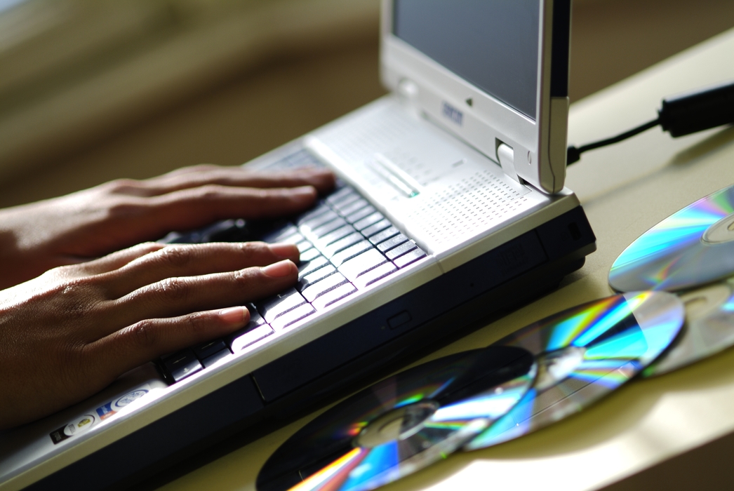 Hands Working on a Laptop Computer with CDs