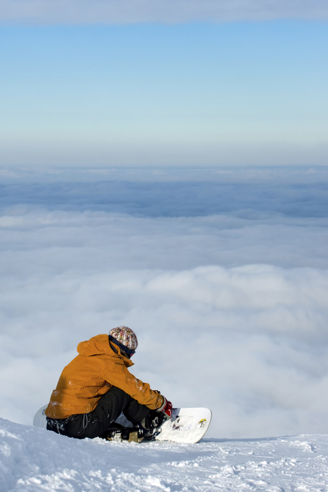Snowboarder siting on top of mountain watching the sky below